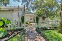 Continue on the terra-cotta tile walkway through the arbor to another patio garden area, enclosed with a charming white picket fence.