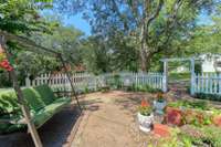 The charming picket fencing, perimeter landscape beds, and shade from the storybook tree in the center of the yard creates a picturesque garden setting.