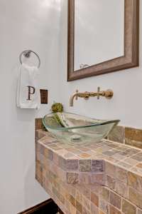 Prepare to impress your guests w/ the stunning half bath featuring a floating natural stone tile vanity, a sleek glass vessel sink & a contemporary wall-mounted faucet. A framed mirror, designer light fixture, & hardwood floors add warmth.