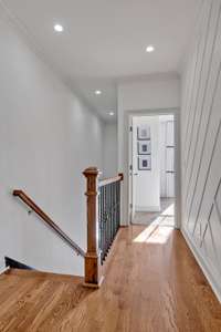 The upstairs hallway is exquisite, featuring stunning hardwood floors, a designer wood accent wall, pristine white paint, and an elegant iron baluster railing.