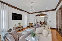 Sunlight floods this inviting space, enhanced by floor-to-ceiling window draperies, arched doorways, and captivating views into the elegant dining room.