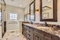 The primary bath features a double vanity, designer stained glass sconces, a stone countertop and upscaled tile floor