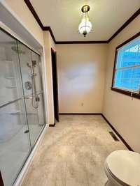 Large area with a linen closet, toilet and LG standing shower and a window.