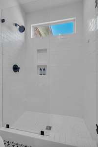 Bright, white walk-in shower space with a transom window for light.