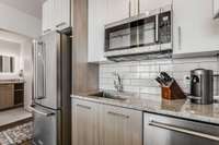 A neutral color palette dominates the kitchen, creating a modern and timeless look. White upper and light woodgrain lower cabinetry, paired with Brazilian granite countertops and stainless steel appliances, contribute to an airy atmosphere