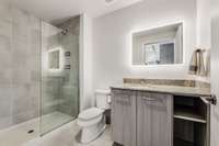 The full bathroom offers a European-style glass shower, Brazilian granite countertops, and a backlit mirror