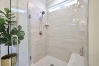 Large walk in tiled shower, glass door & bench.