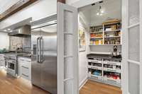 A large, walk-in pantry features frosted glass double doors and pull out shelves reinforced to support a 250 pound load.