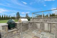 The outdoor kitchen features a built-in grill, refrigerator and plenty of custom stone work, along with continuing the Blue Stone tile from the upper patio.