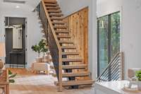 Second floor view of the floating staircase, a wall of windows, and looking into the primary bedroom entrance