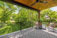 Covered patio off of the primary bedroom, with custom metal railing and a wood paneled ceiling and ceiling fan.