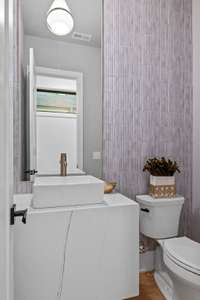 Half bath with a floating quartz vanity, tiled accent wall, a custom mirror and beautiful lighting