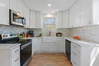 Bright kitchen with stainless appliances, farm sink, quartz countertops and decorative tile backsplash.