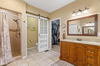 PRIMARY BATHROOM WITH VIEW OF SHOWER AND LARGE PRIMARY CLOSET ENTRANCE TO LARGE CLOSET