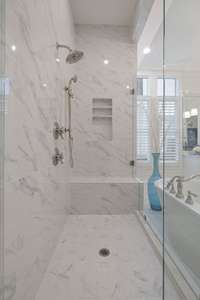large frameless shower with multiple shower heads and a bench for ease