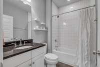 This bathroom offers a shower tub combination with clean neutral tiles and granite countertops.
