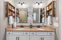 Refresh and rejuvenate in this primary suite's ensuite bath, where crisp white cabinetry and earthy granite tops meet rustic wood accents, blending farmhouse charm with modern luxury.