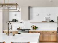 Designer light fixtures, fully tiled wall, open shelves, and built-in range hood in the kitchen