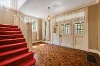 Large entry foyer with solid wood and beveled glass front door with hand laid Teak wood flooring and antique glass light fixture.