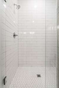 There is a large tile shower with frameless glass doors.