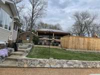 As you come to the back in front of the 3 car garage - this is what you see. Stone wall is so striking to the eye. The fence surrounds an inground pool. Straight ahead you see a room with roof - that is the outdoor covered kitchen. OH, what fun!!!