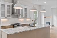 Notice the Quartzite square tiled backsplash that falls below the stainless steel, box canopy chimney vent-a-hood, creating an inverted “T”, flanked on opposite sides by wall cabinets, accented with glass doors and under cabinet lighting.