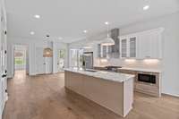 Everyone loves the varied uses for a kitchen island set off by bar stools. It's easy to serve from and become a workstation. The 1st Floor Bedroom En Suite entrance is pictured in the distance at the open doorway on far left.