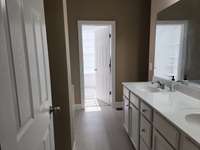 Master bath with double vanities and open door leading to walk-in closet