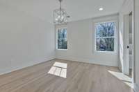 This bedroom has a central chandelier & four recessed LED can lights. Two large double-hung windows invite warm natural light, reflected off shimmering white painted trim.