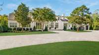 View of the front of the estate boasting the cedar shake roof, German schmear technique brick application, lush landscaping, and a large European-style driveway.