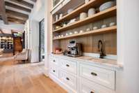 Custom built coffee bar featuring open shelving, extra storage, a bar sink, and antiqued brass faucet.