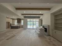 Spacious Great Room featuring a 12' ceiling with wood beam detail and a wood-burning fireplace with cabinet built-ins to each side of fireplace.  Slider doors for easy access to covered outdoor living.  Photo taken 9/18/24