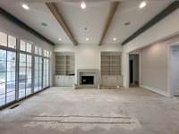 Great Room featuring a 12' ceiling with wood beam detail and a wood-burning fireplace with cabinet built-ins to each side of fireplace.  Slider doors for easy access to covered outdoor living.  *this house is under construction Photo taken 9/18/24