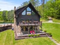 Behold the rear view of the house, showcasing the deck off the kitchen for outdoor dining and relaxation, as well as the porch off the basement bedrooms, providing a serene retreat to enjoy the surrounding nature.