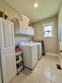 Laundry room has tile floor,overhead cabinets and a tall storage cabinet that will remain w/the home