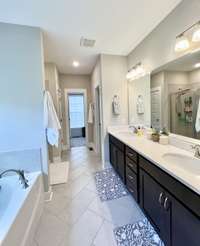 View of large vanity with 2 sinks, quartz countertops, tile floor, garden tub, separate shower