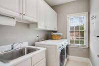Immaculate laundry room with stainless steel sink, and both lower as well as upper cabinet storage.