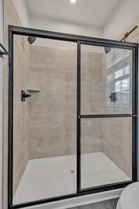 Owner's Shower ~ Upgraded Roman Shower has tile, recessed light, black finish fixtures and glass sliding doors.