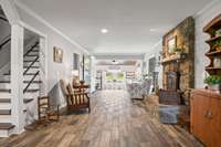 This is a view of the original living room featuring the wood burning fireplace with a large hearth.  The opening on the left just beyond the antique chair/table is the hallway access to the large storage room, utility closet and primary bedroom.