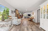 A view looking back at the family room and great room at the top of the steps to the kitchen and dining room area.  Cozy chairs are placed in front of a large window with a view of the back yard and hardscape patio.