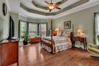 Primary bedroom with newer wood floors, triple crown molding and ceiling fan