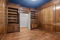 Storage areas flank the entrance of the wood-paneled office, providing both functionality and style.