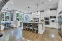 Expansive eat in kitchen with island and large windows showcasing the beautiful wooded property.