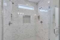 Large shower with built in penny tile niches for storage, window provides natural light, dual shower heads and frameless glass