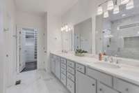 Primary bathroom features dual vanities, wood cabinetry and beautiful tile work in the shower and floors.