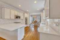 Kitchen features white cabinetry and counter tops with chevron backsplash and brick accent wall