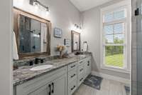 Primary Suite Bathroom, overlooking the front yard, with marble countertops, tile floors & shower, and comfort-height toilet.