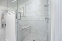 Tile shower with marble bench and glass doors with hidden niche for products.