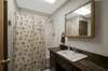 Main bathroom with full tub/shower combo, single sink, linen closet and two hanging wall cabinets.