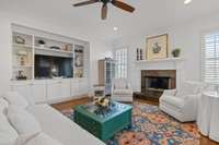 A few steps into the home find cozy living in the white and bright Den featuring gas fireplace and built in shelving overlooking the side covered porch